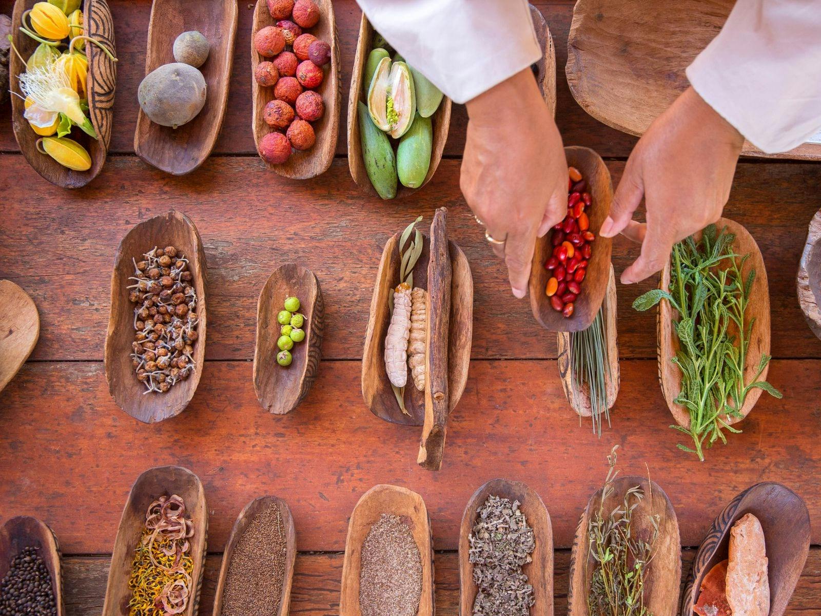 Wooden Coolamons holding bush foods with hands holding one