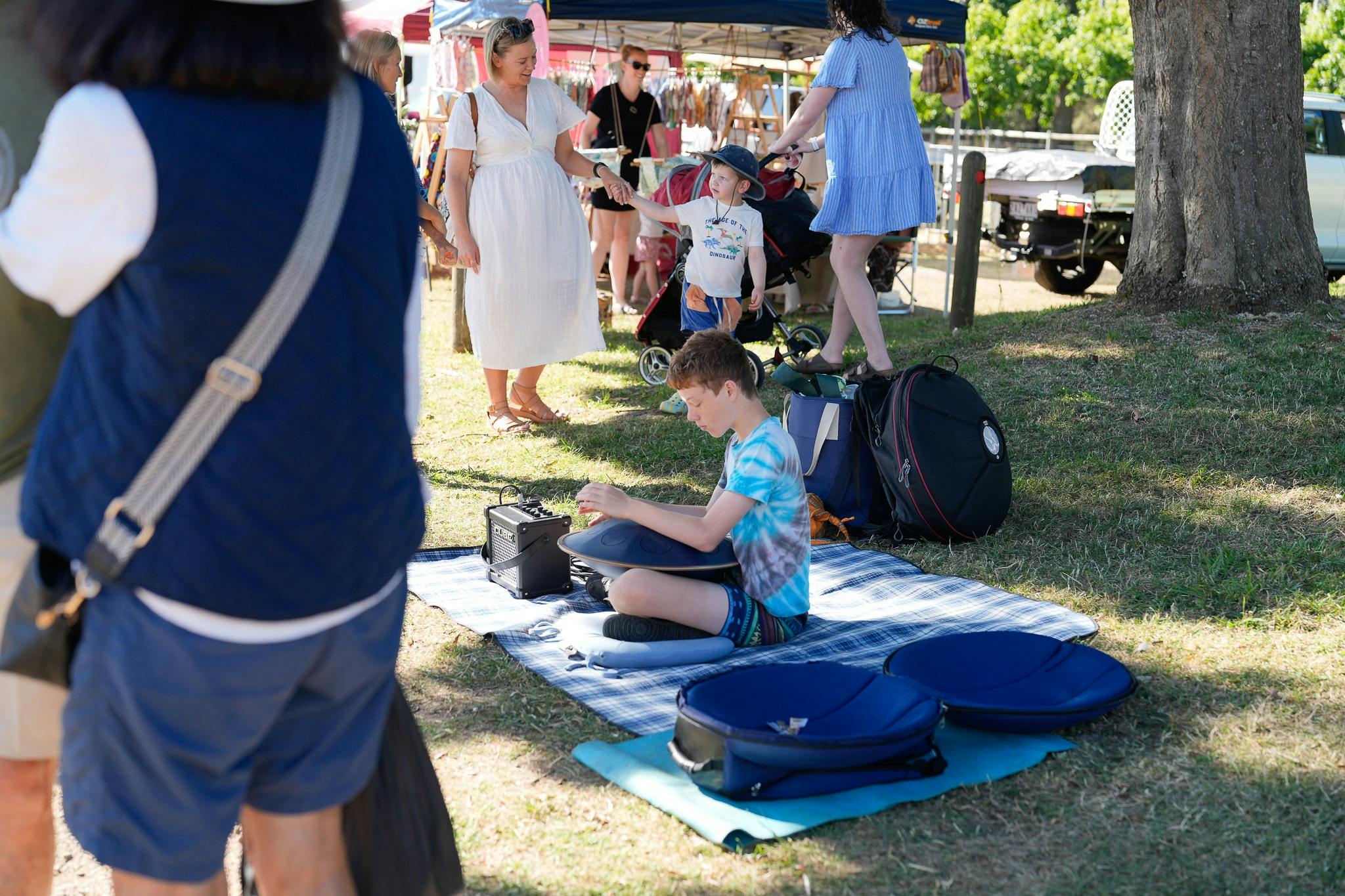 boy busker playing is electric steel drums. Here he is sitting under a tree in the shade playing