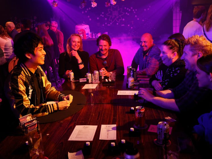 Several people are seated around a table looking at a Japanese magician, also seated at the table