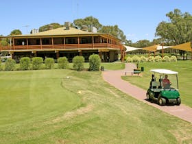 Golf clubhouse with manicured lawns and person on a golf cart on a path