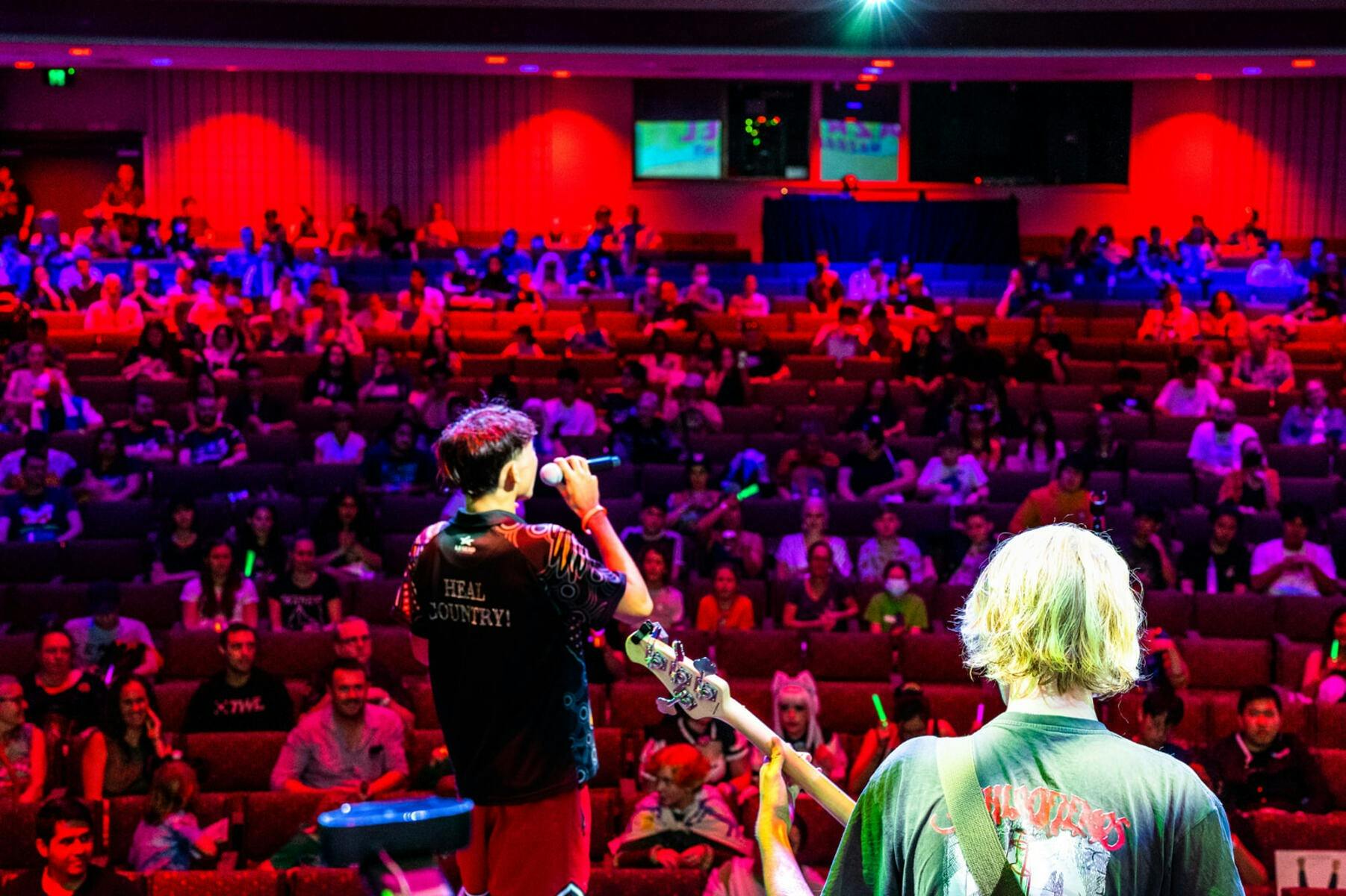 A performer on stage in front of a large crowd under red and purple lights at a gaming festival