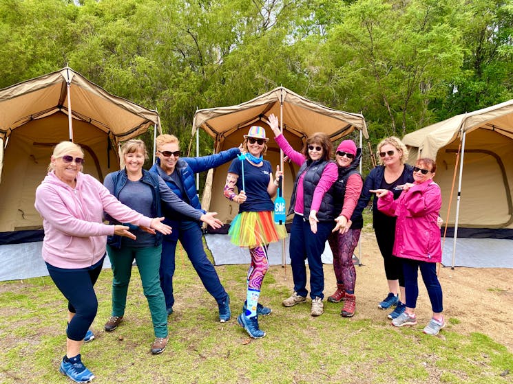8 women standing with arms toward the middle in a campground