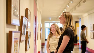 Two women view artwork in gallery.