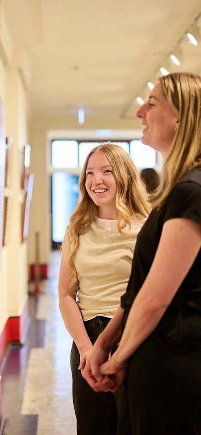 Two women view artwork in gallery.