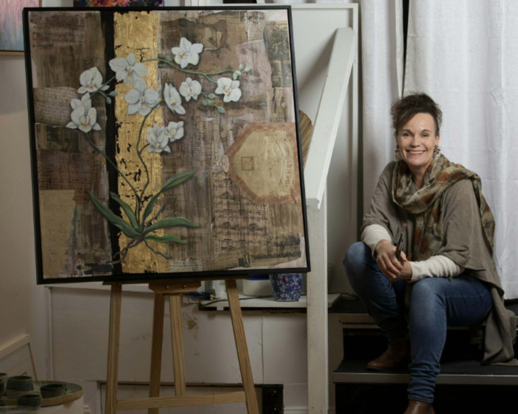 Woman sitting, smiling next to artwork