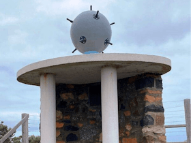A stone curved memorial to two soldiers killed in WW2 while disabling a mine. There is a mine on top