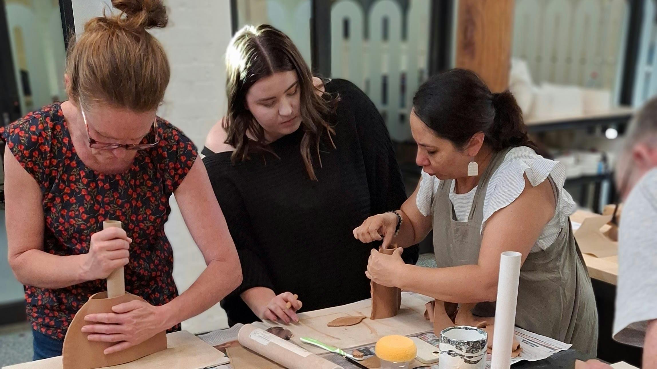 three people learning to make a vase out of clay