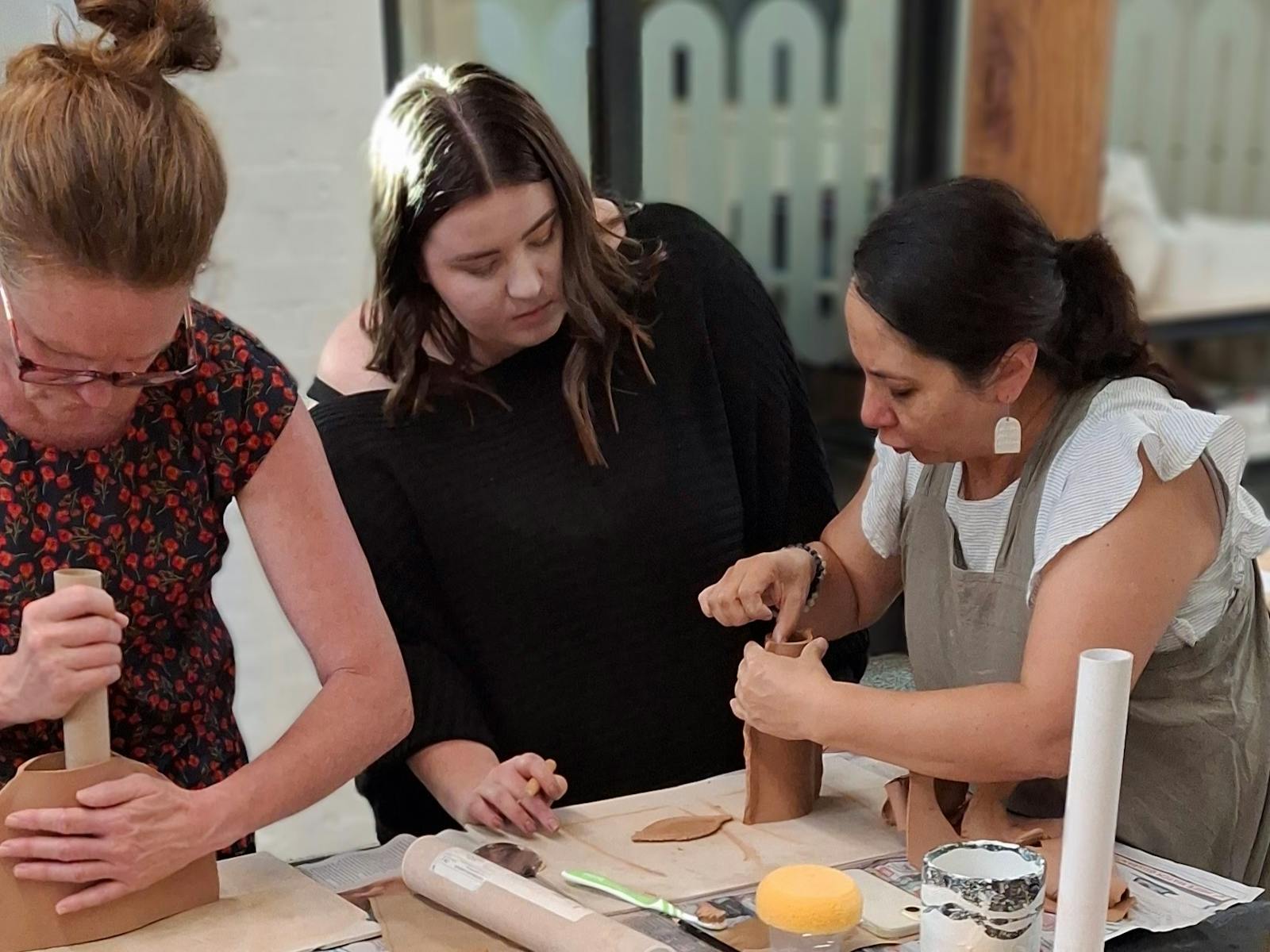 three people learning to make a vase out of clay