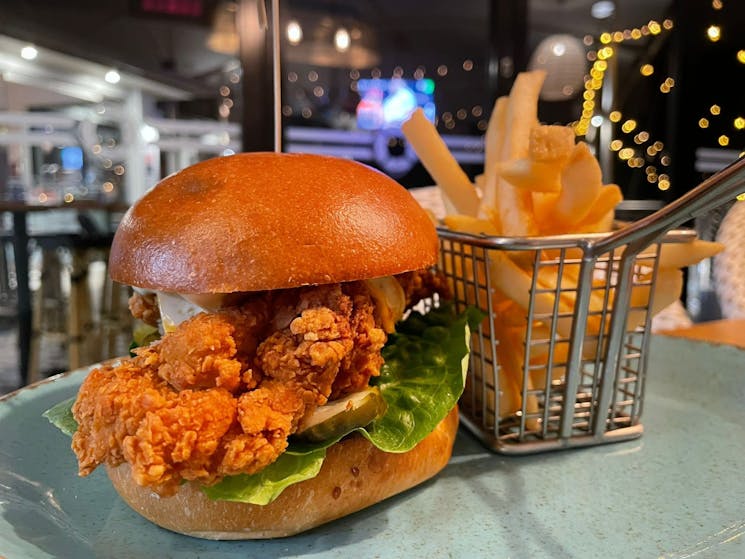Close up image of a crispy fried chicken burger, with potato chips on the side