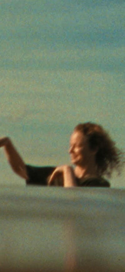 Woman in bathing suit standing in water leaning back with another woman flicking water at her