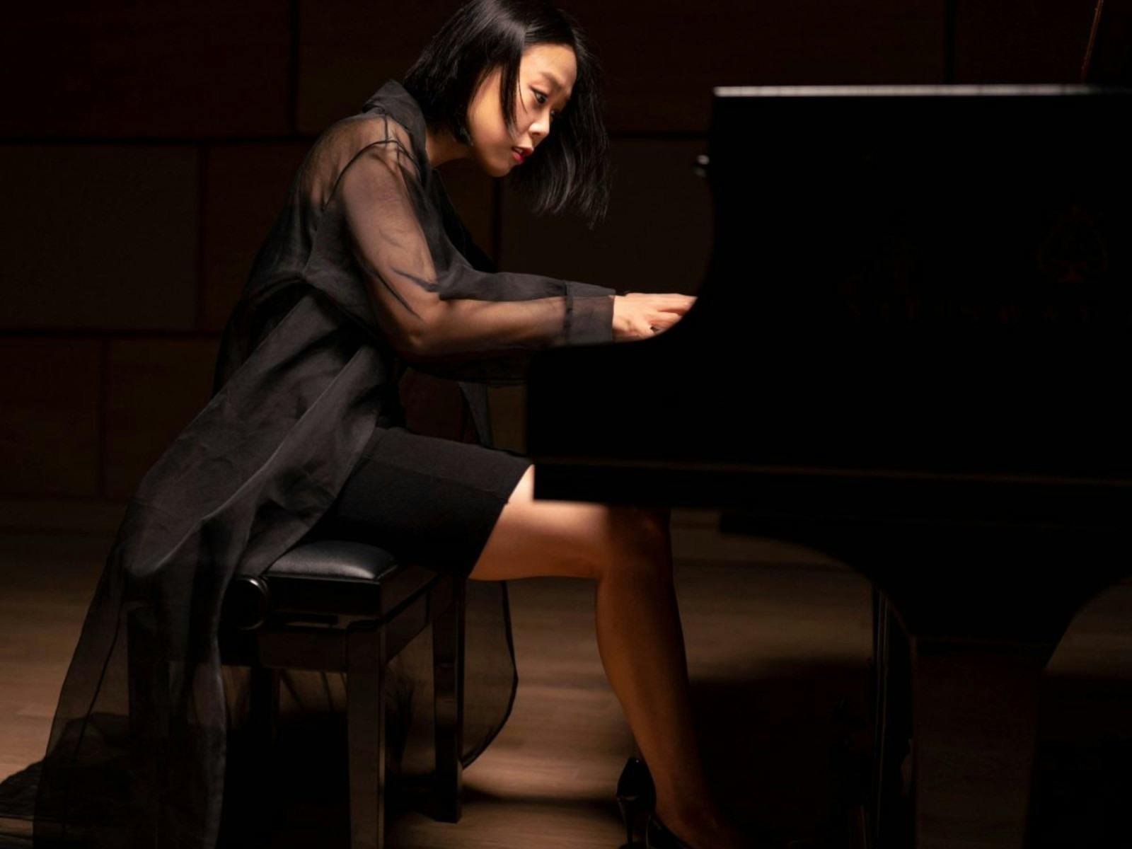 Photo of a musician, wearing a black dress, playing a grand piano.
