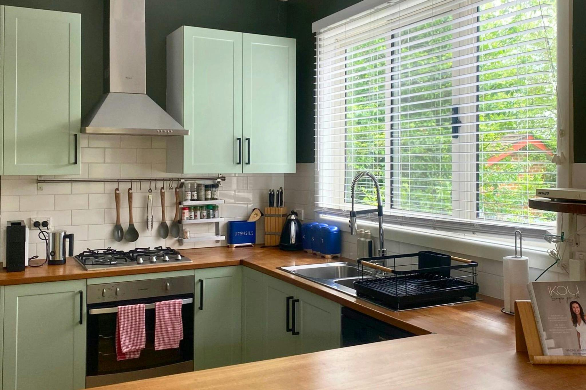 Fully equipped kitchen with sage green cabinetry and views of the cottage garden.