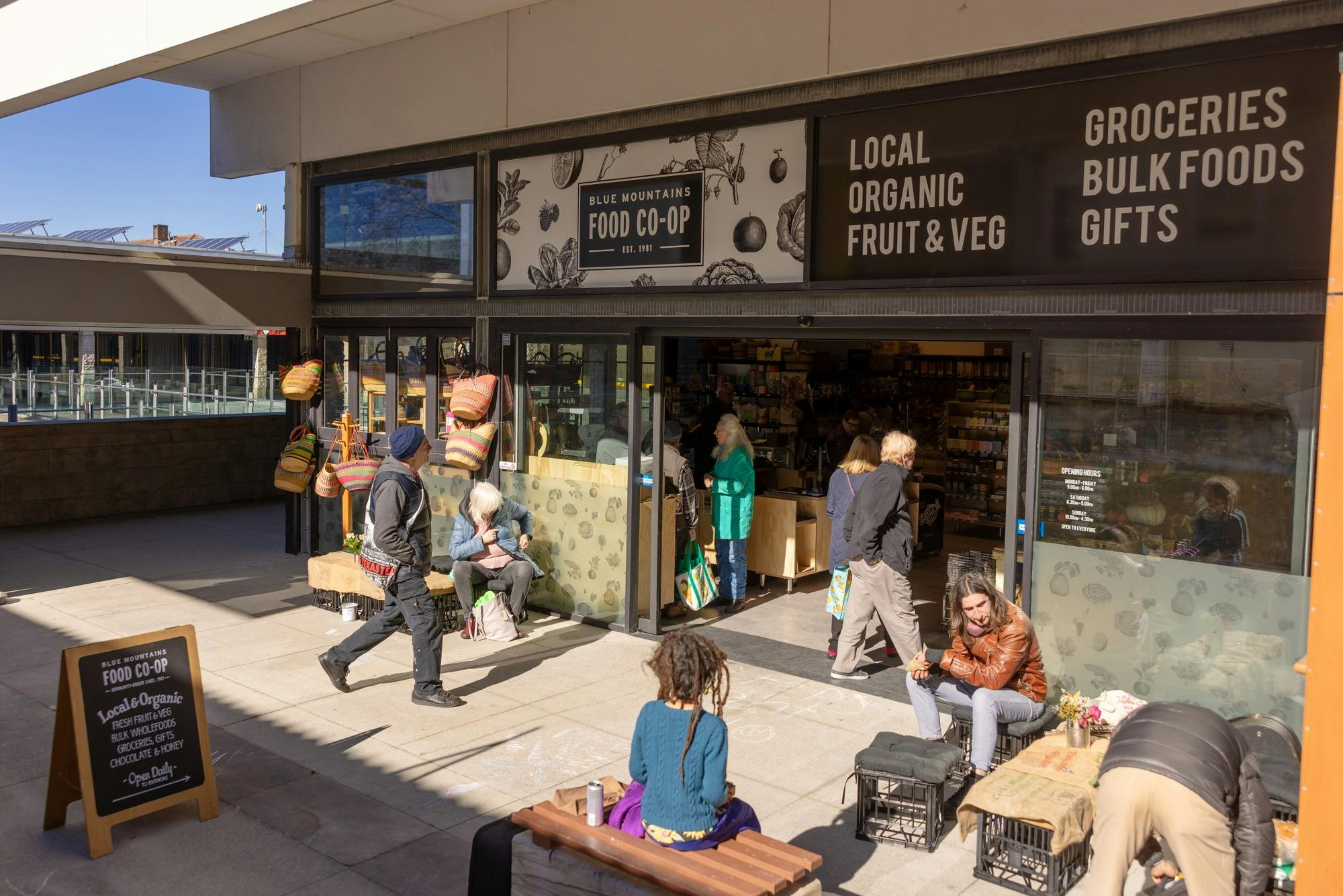Outside of the Co-op featuring people entering sliding doors and people sitting on benches out the f