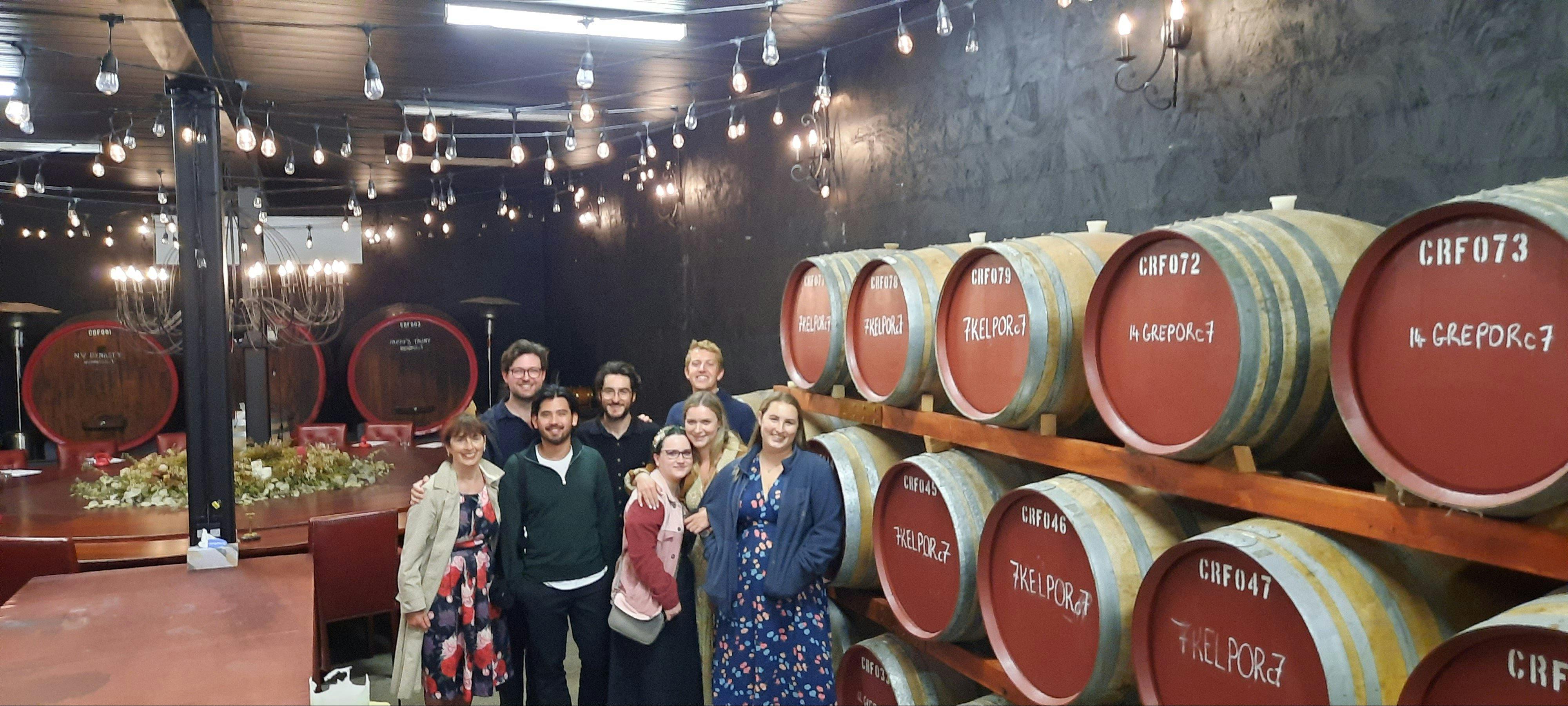 7 people in a barrel room with hanging lights.
