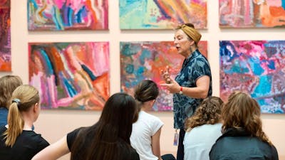 Photograph of speaker gesturing at colourful artwork in front of group