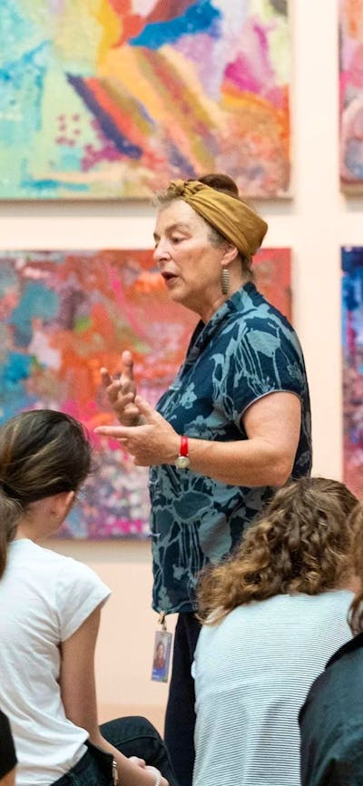 Photograph of speaker gesturing at colourful artwork in front of group