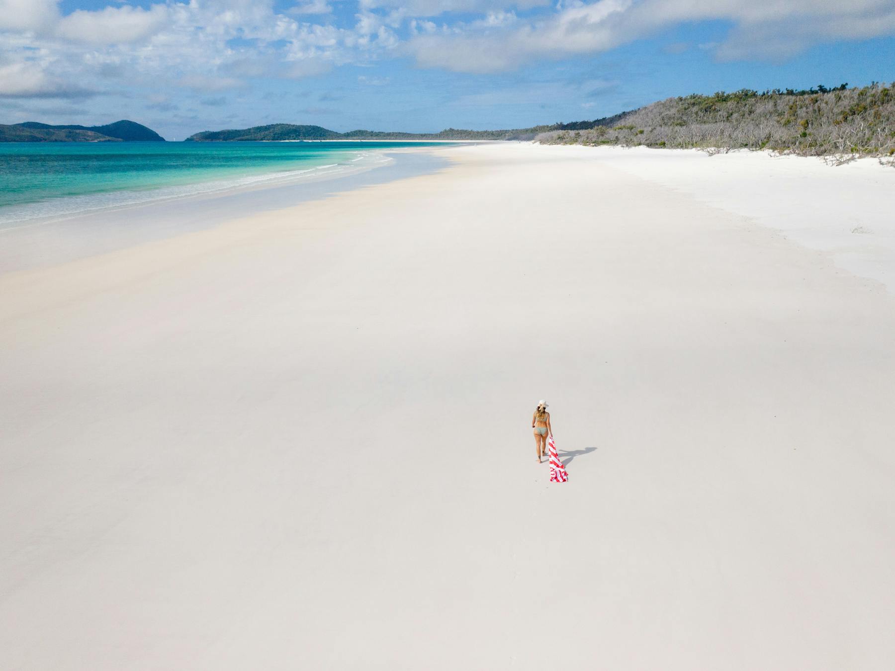 A woman strolling along the wide and long white silky beach