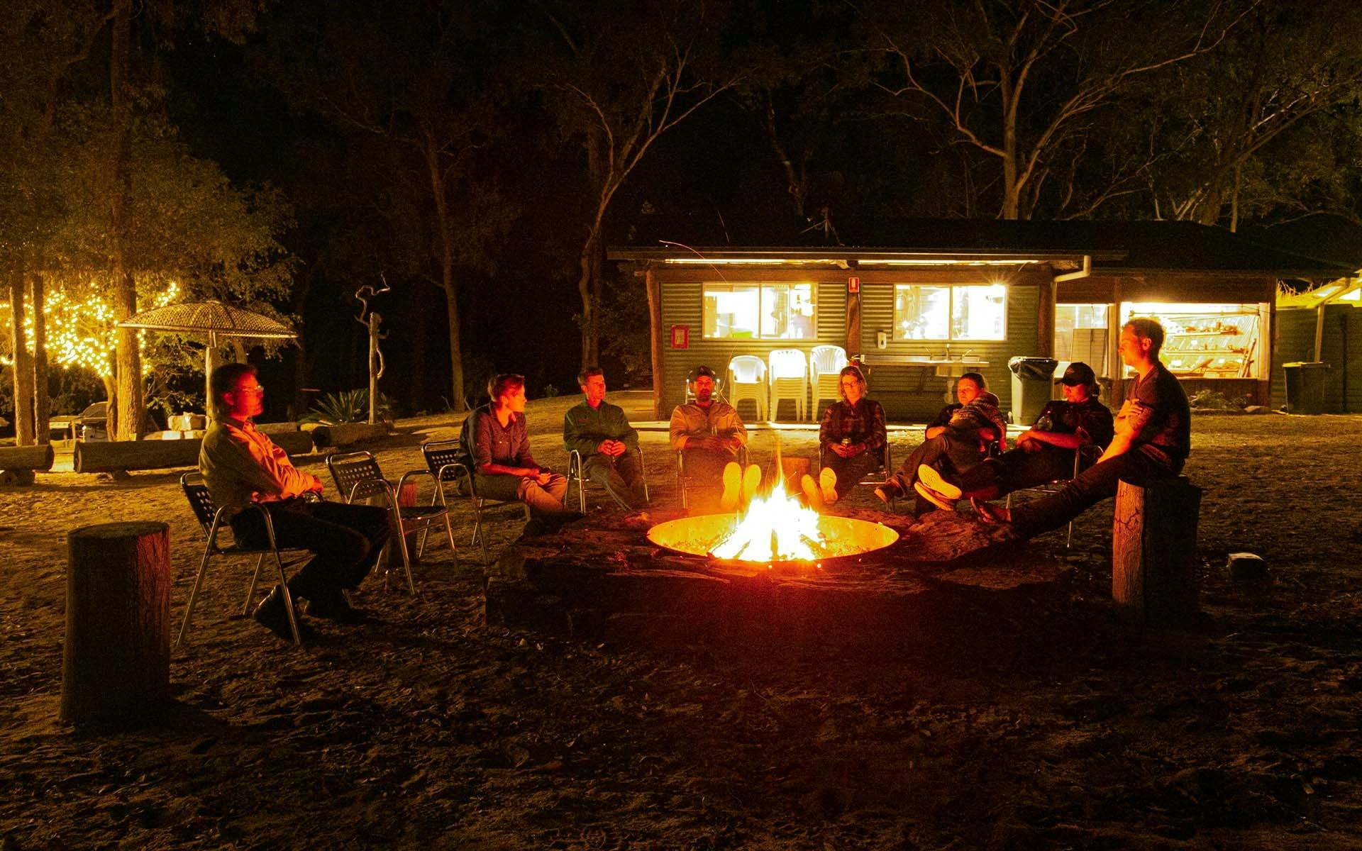 A group of guests sitting around a campfire in the bush at night