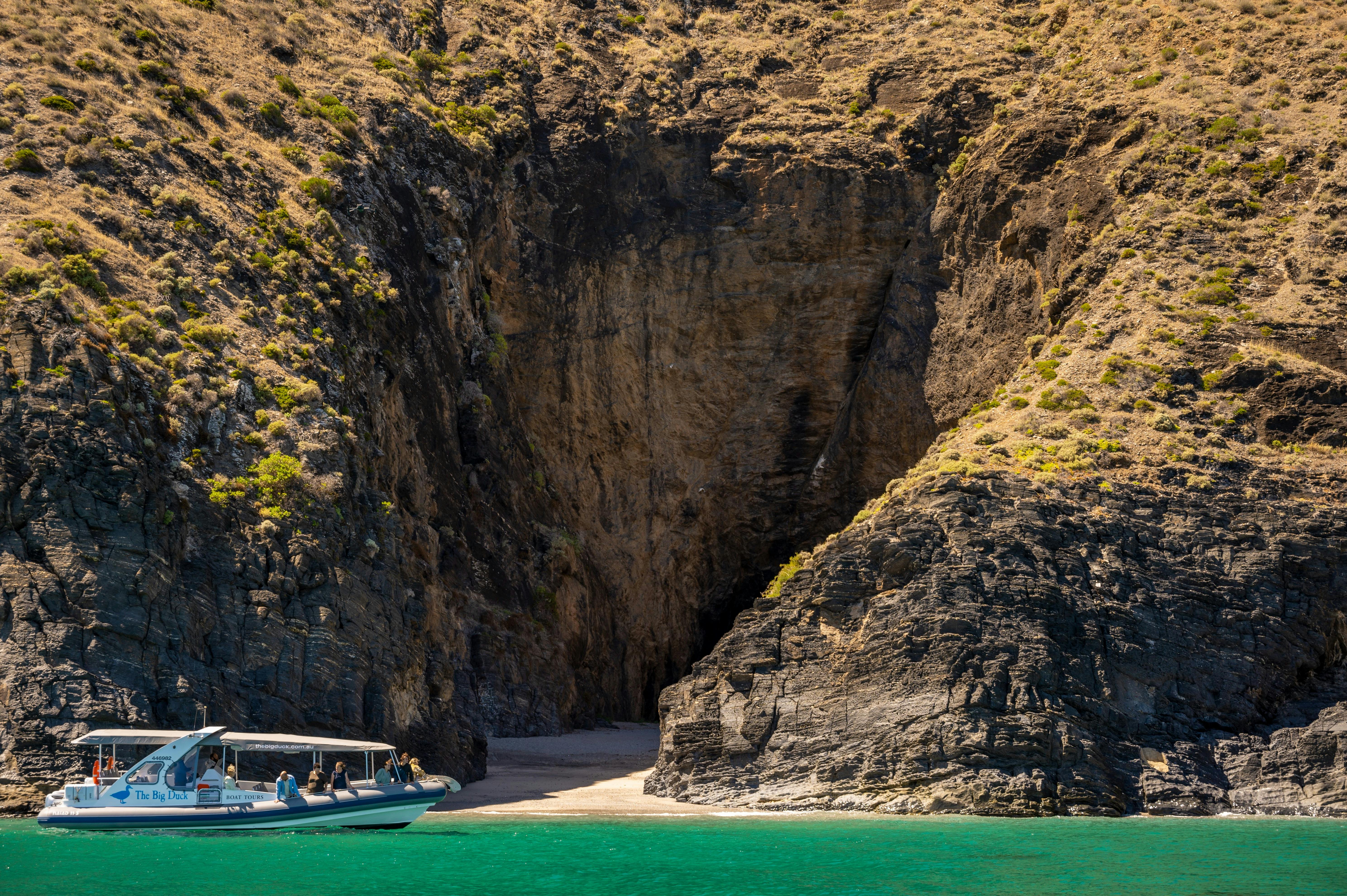 A boat cruises on clear turquoise water near a rocky shoreline and small sandy cove.