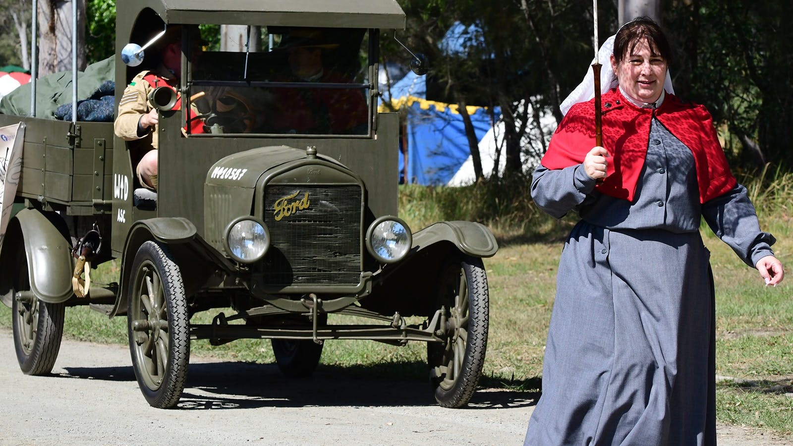 A lady dressed as a WW1 Nurse with a parasol leads a WW1 Vehicle A lady dressed as a WW1 Nurse with a parasol leads a WW1 Vehicle