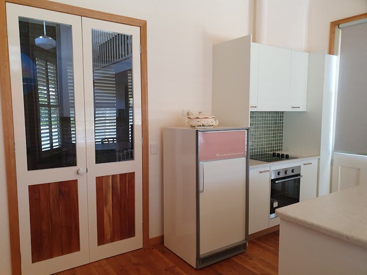 Corner kitchen with a light pink and white fridge and oven/cooktop with white and wood double doors