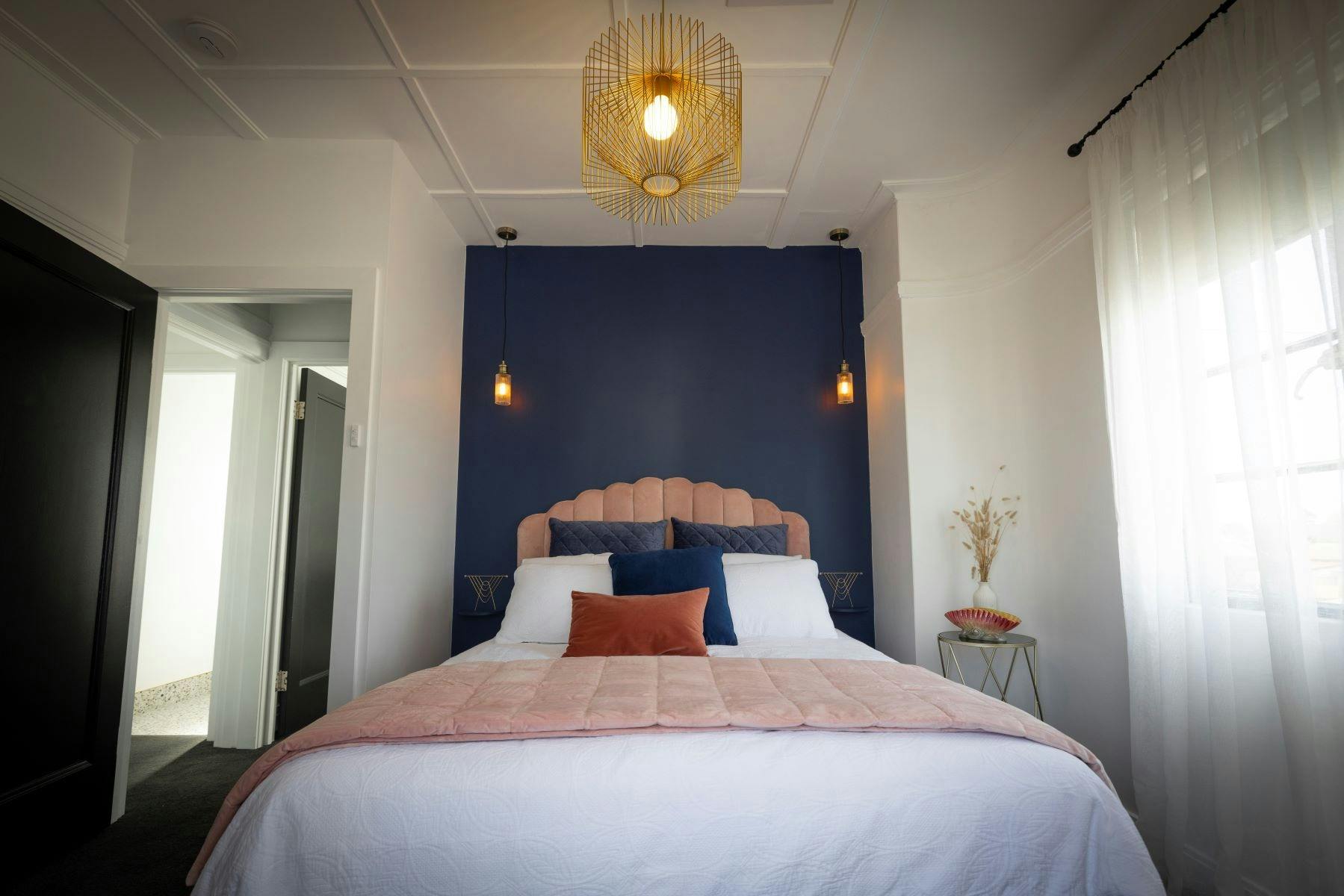 A cosy, sumptuous room with queen size bed, art deco stylinng, a navy feature wall & pendant light.