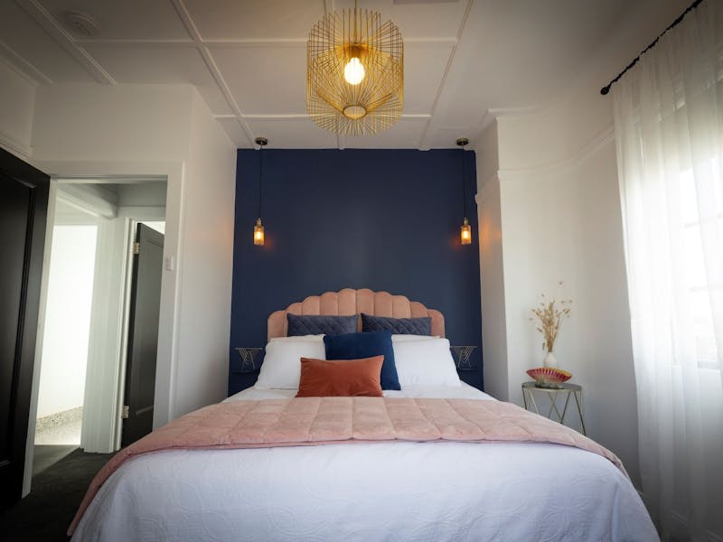 A cosy, sumptuous room with queen size bed, art deco stylinng, a navy feature wall & pendant light.