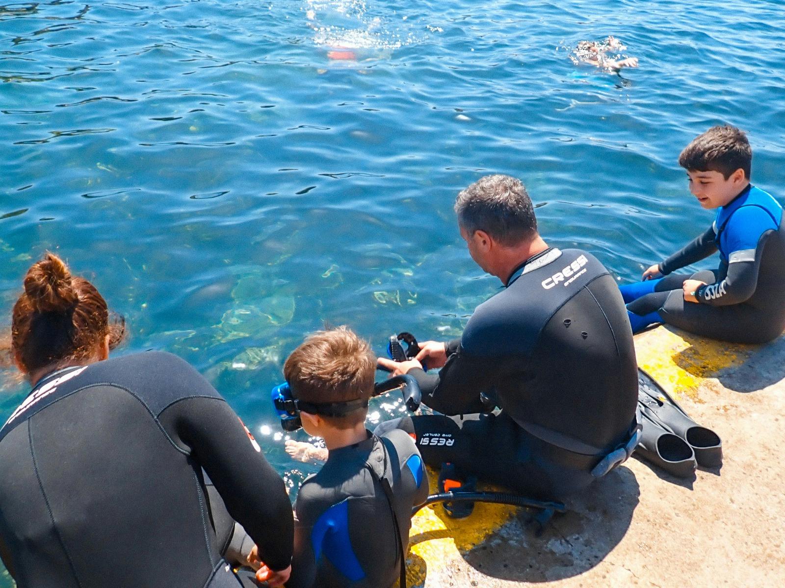 Two parents and two kids sit on the ledge at Clovelly Beach, putting on snorkelling gear