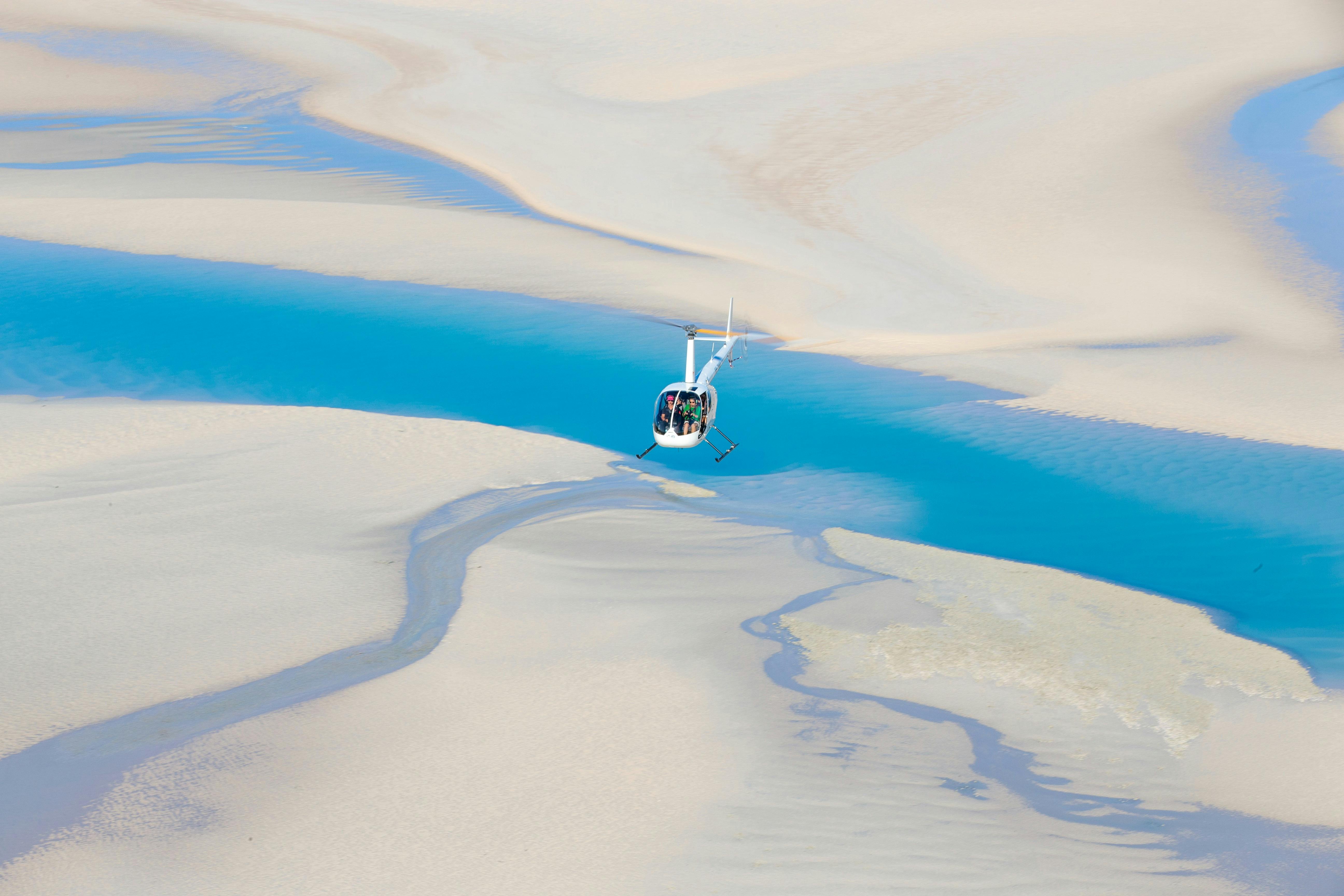 A white helicopter flies over sandbars and blue creek