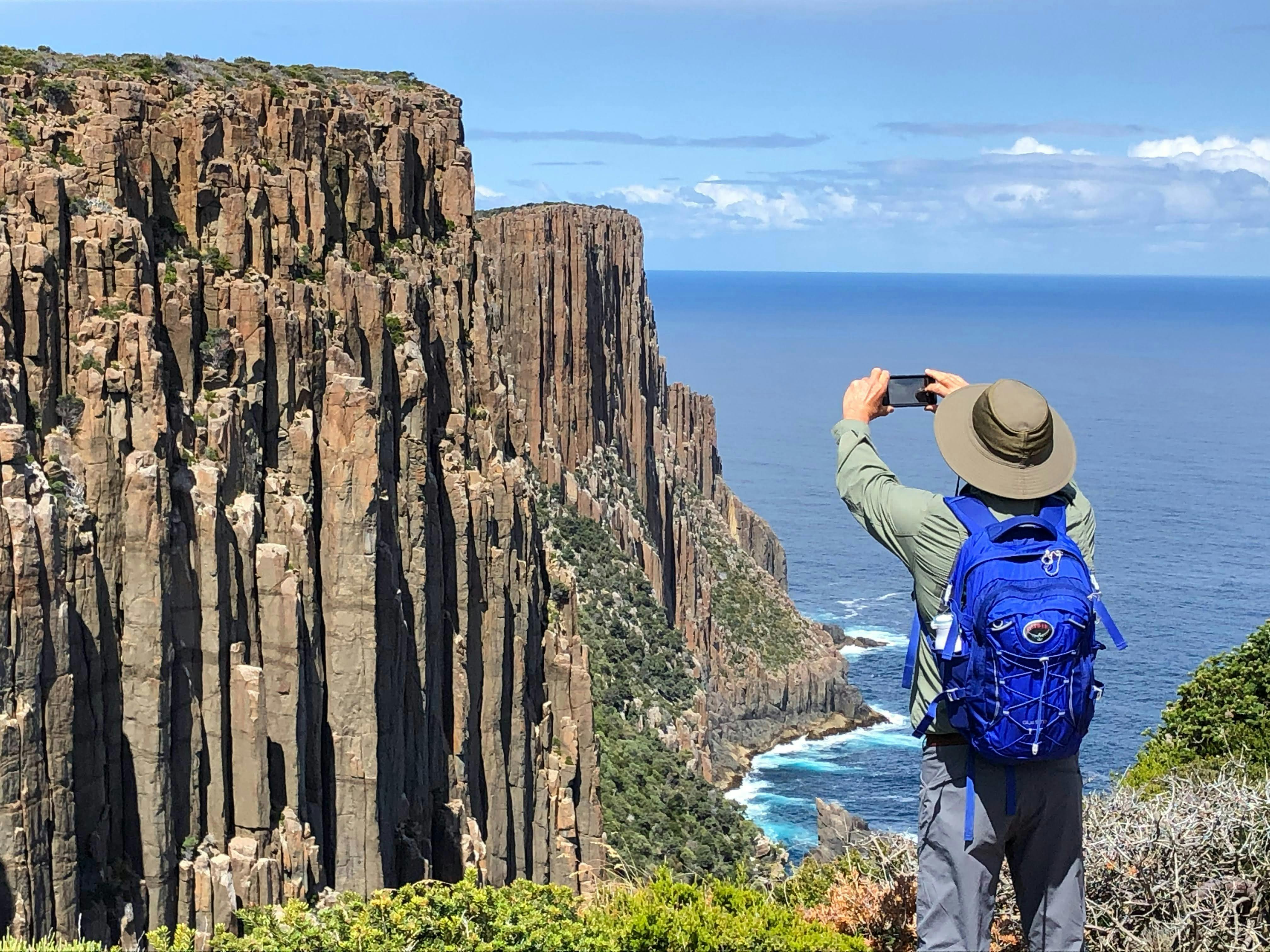 Guest photographing dramatic sea cliffs on the Three Capes Walk Tasmania during a pack free guided w