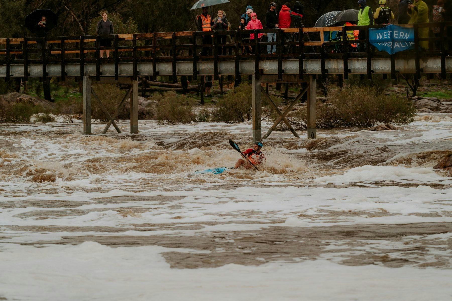 Paddler in rapids with spectators on the bridge