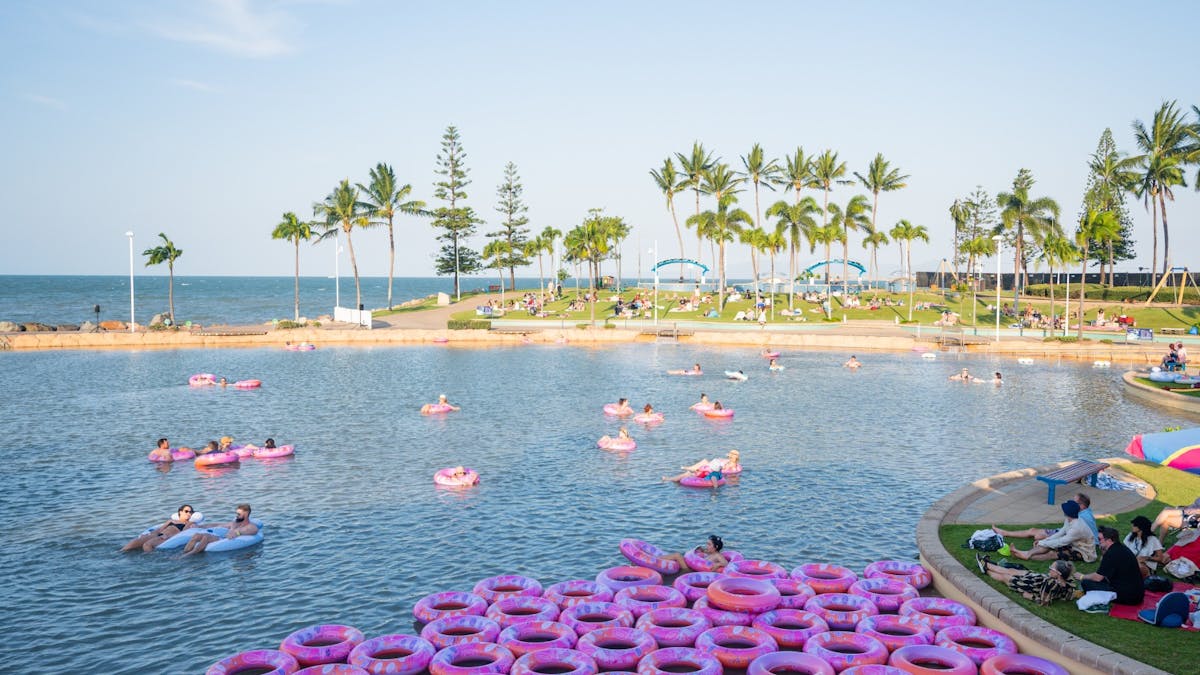 People floating on pink inflatable rings in a large seaside lagoon at The Strand in Townsville.