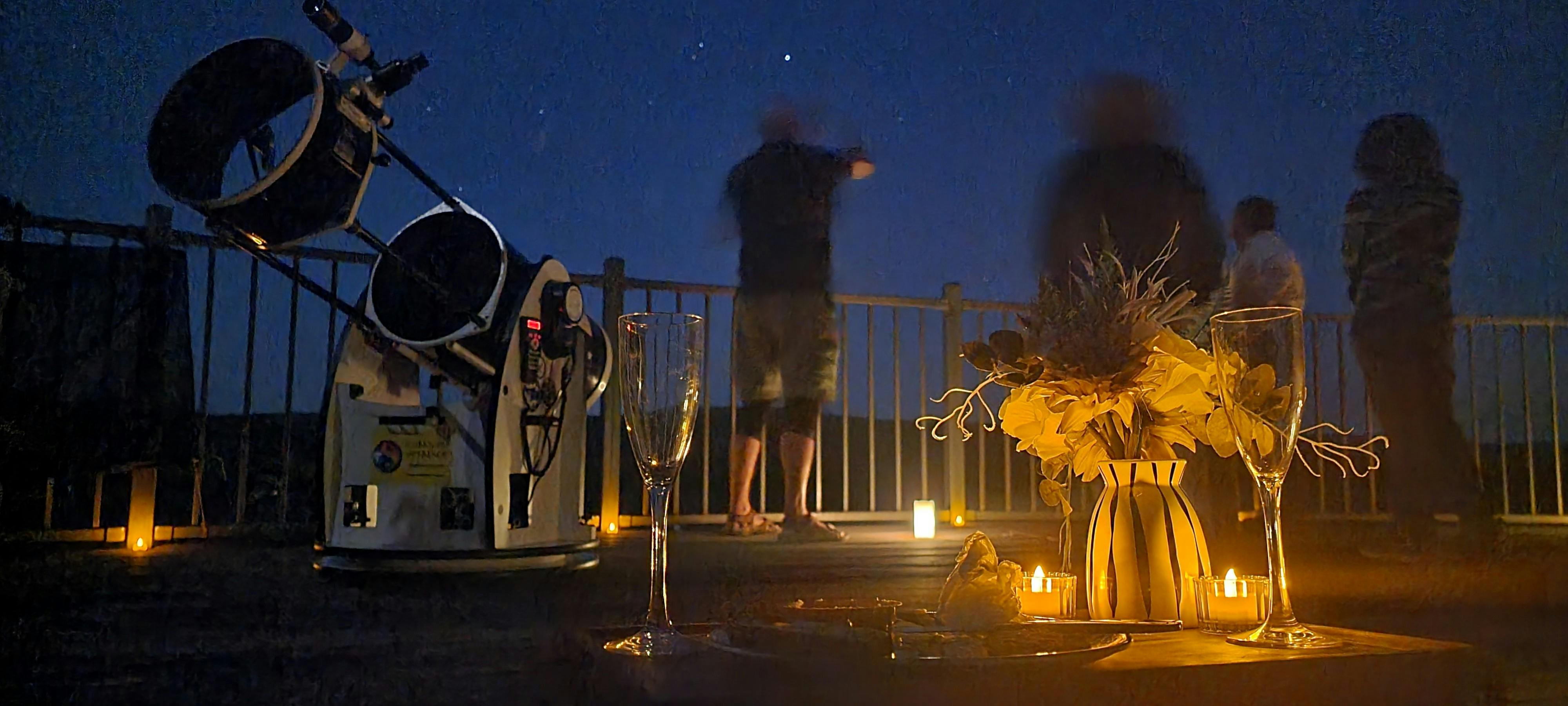 Hikers looking out at stary night sky with large telescope. Candles create warm atmosphere