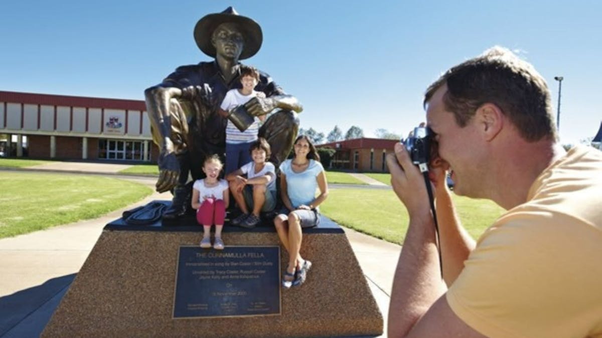 Man taking photo of his family sitting on the Cunnamulla Fella Statue