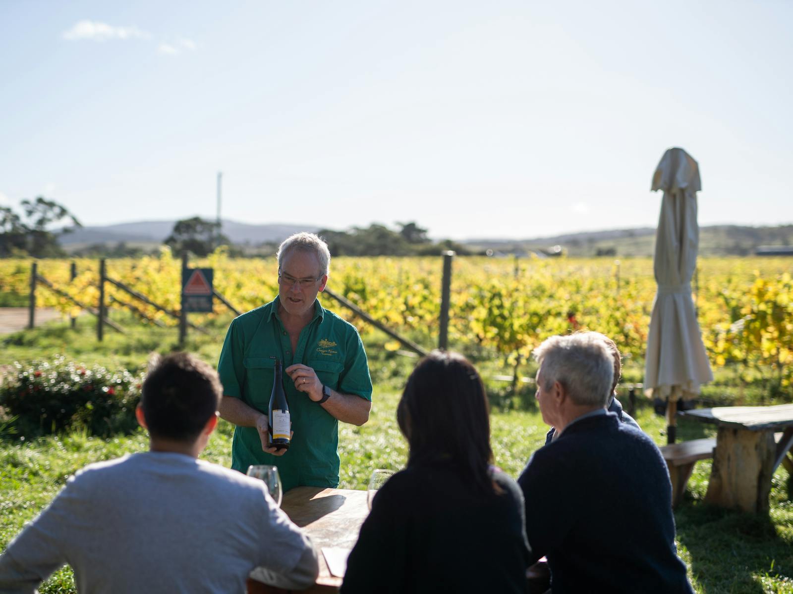 Glenn Travers, Craigie Knowe owner, offering guests a wine tasting, outdoors at a table in the vines