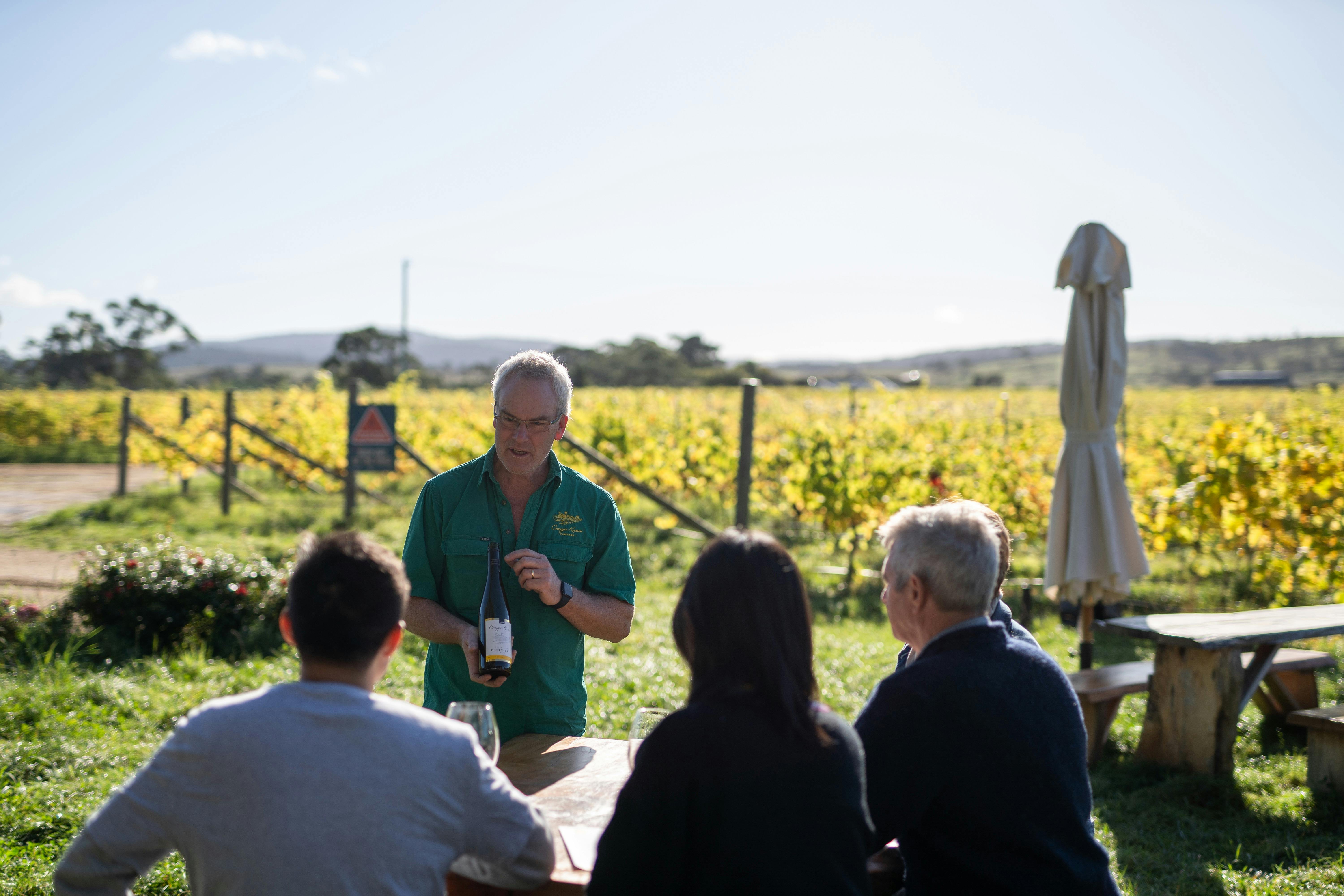 Glenn Travers, Craigie Knowe owner, offering guests a wine tasting, outdoors at a table in the vines