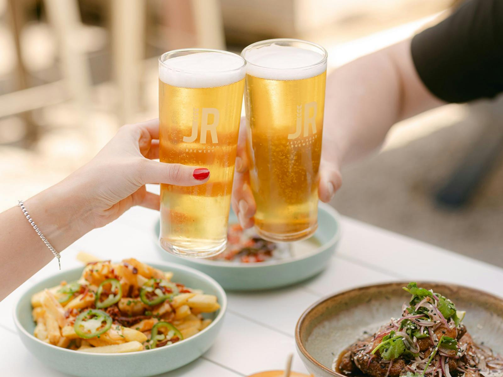 Two hands holding Jetty Road pints of beer cheersing