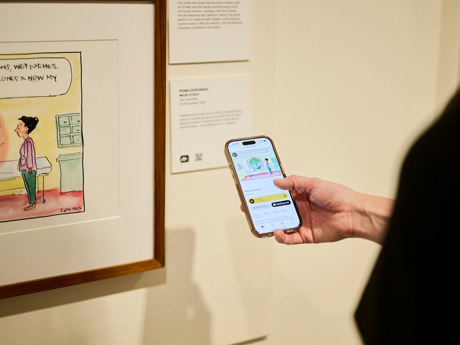 Phone shows audio description of political cartoon in gallery.