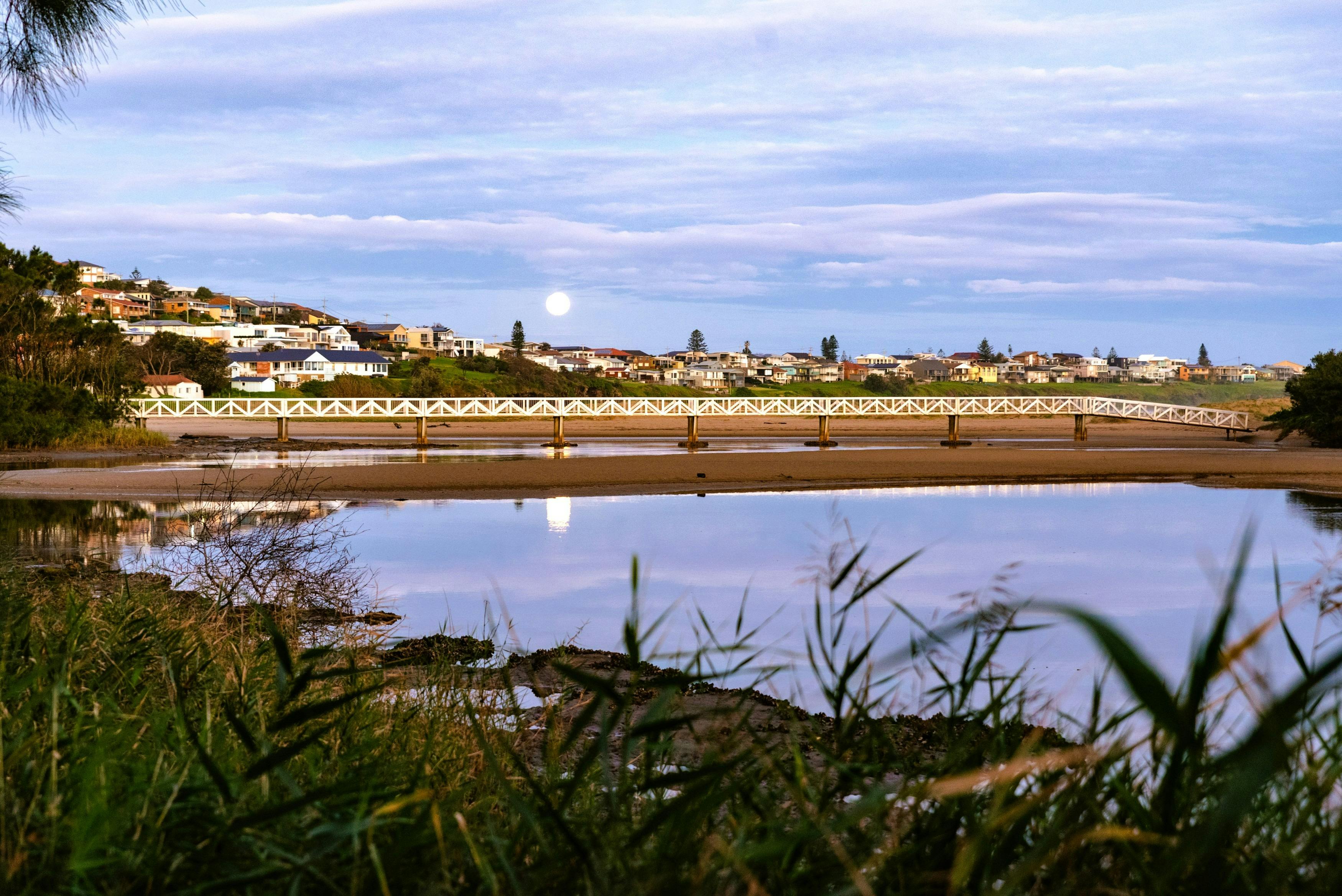 Moon rises over a river inlet with footbridge in foreground