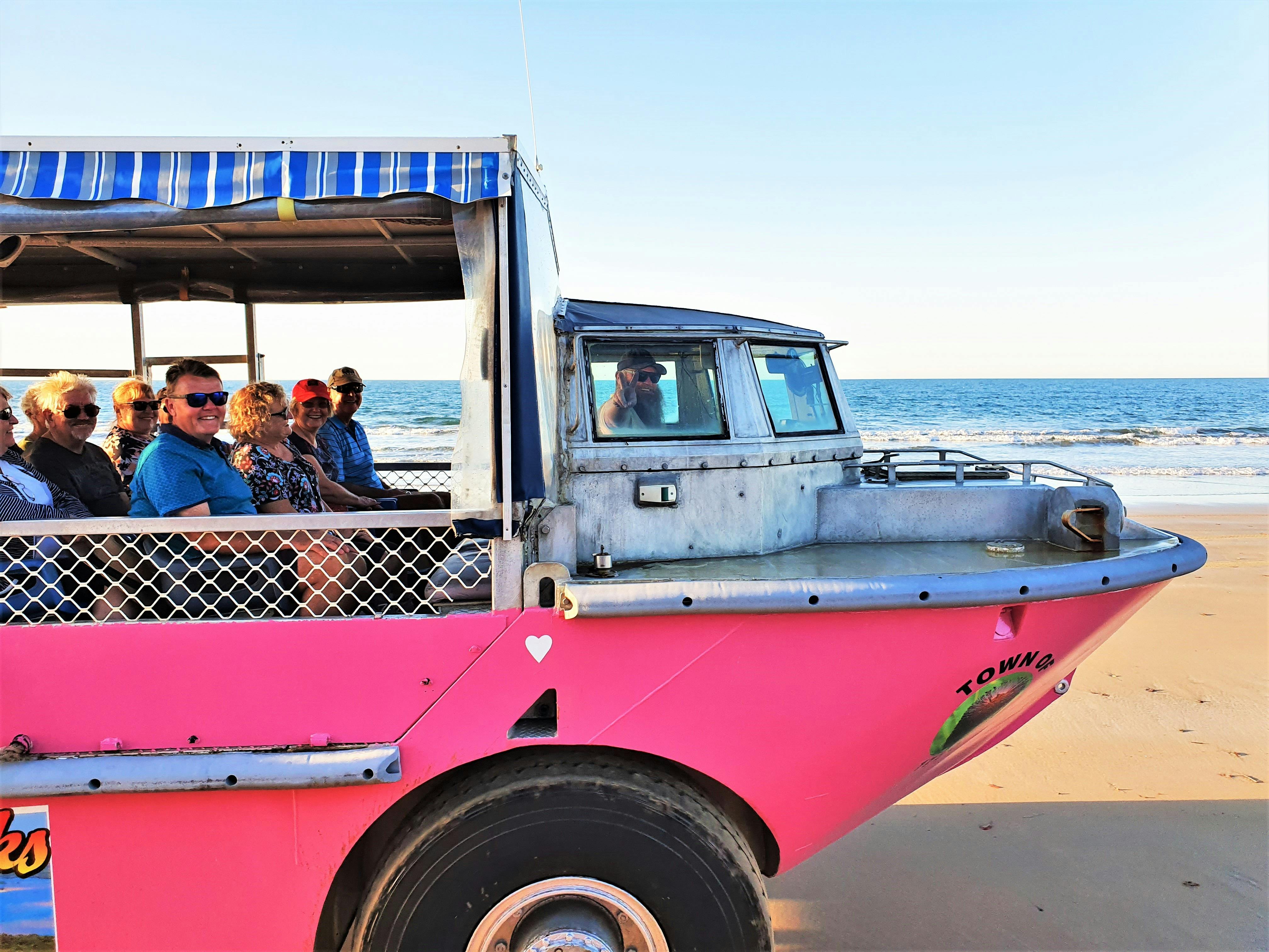 Smiling guests are seated on board pink amphibious vehicle travelling along beach