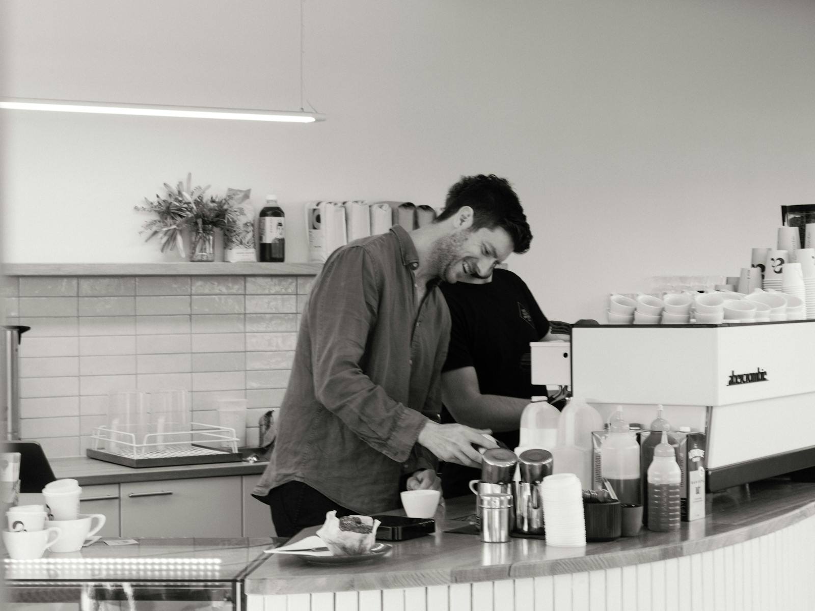 A man smiles as he prepares a coffee behind the counter of Abercrombie Coffee.