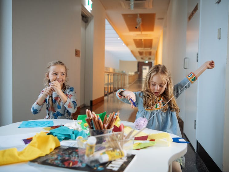 Two young girls at an activity table in an art museum with scissors, wool and paper