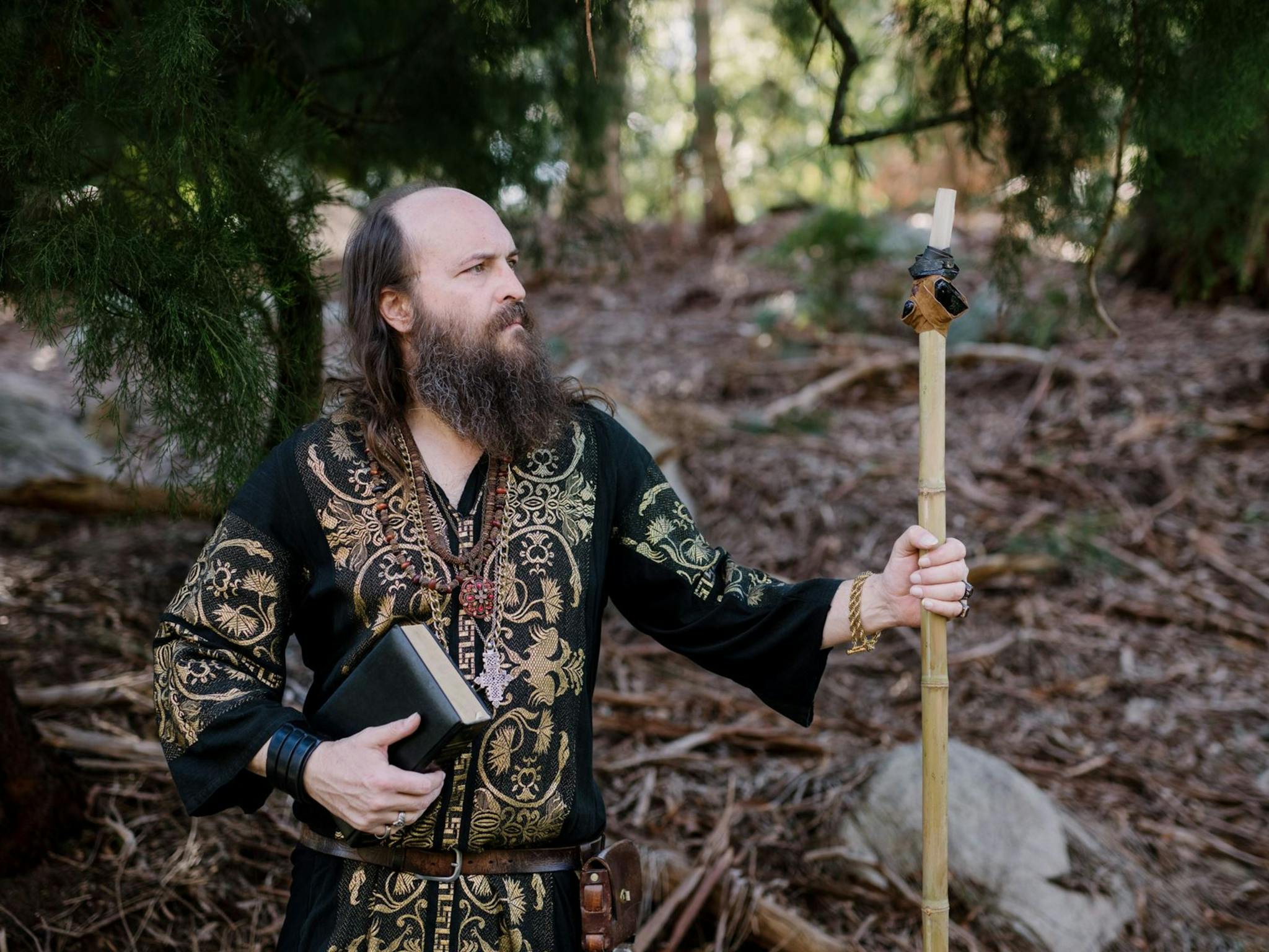 A man with a beard in intricate clothing, holding a book and staff