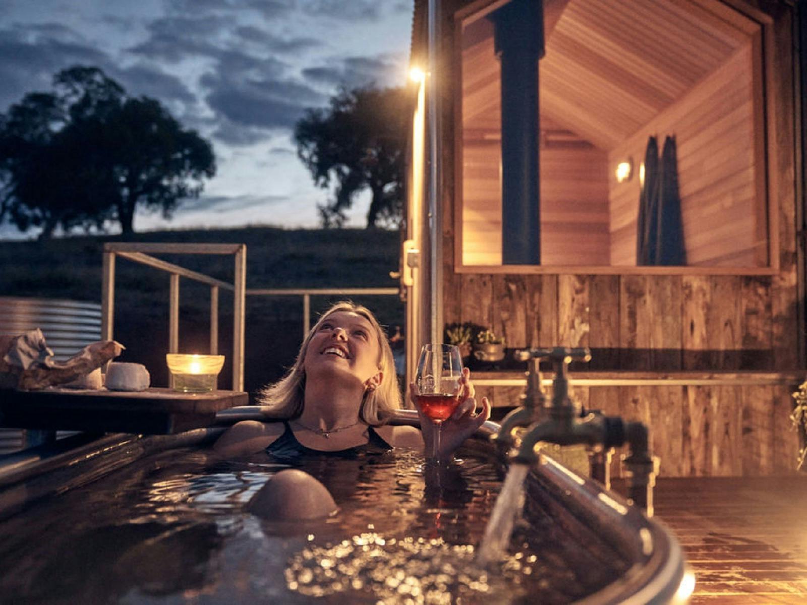 A lady looking up into the stars whilst sitting in the outdoor bath with a glass of red wine