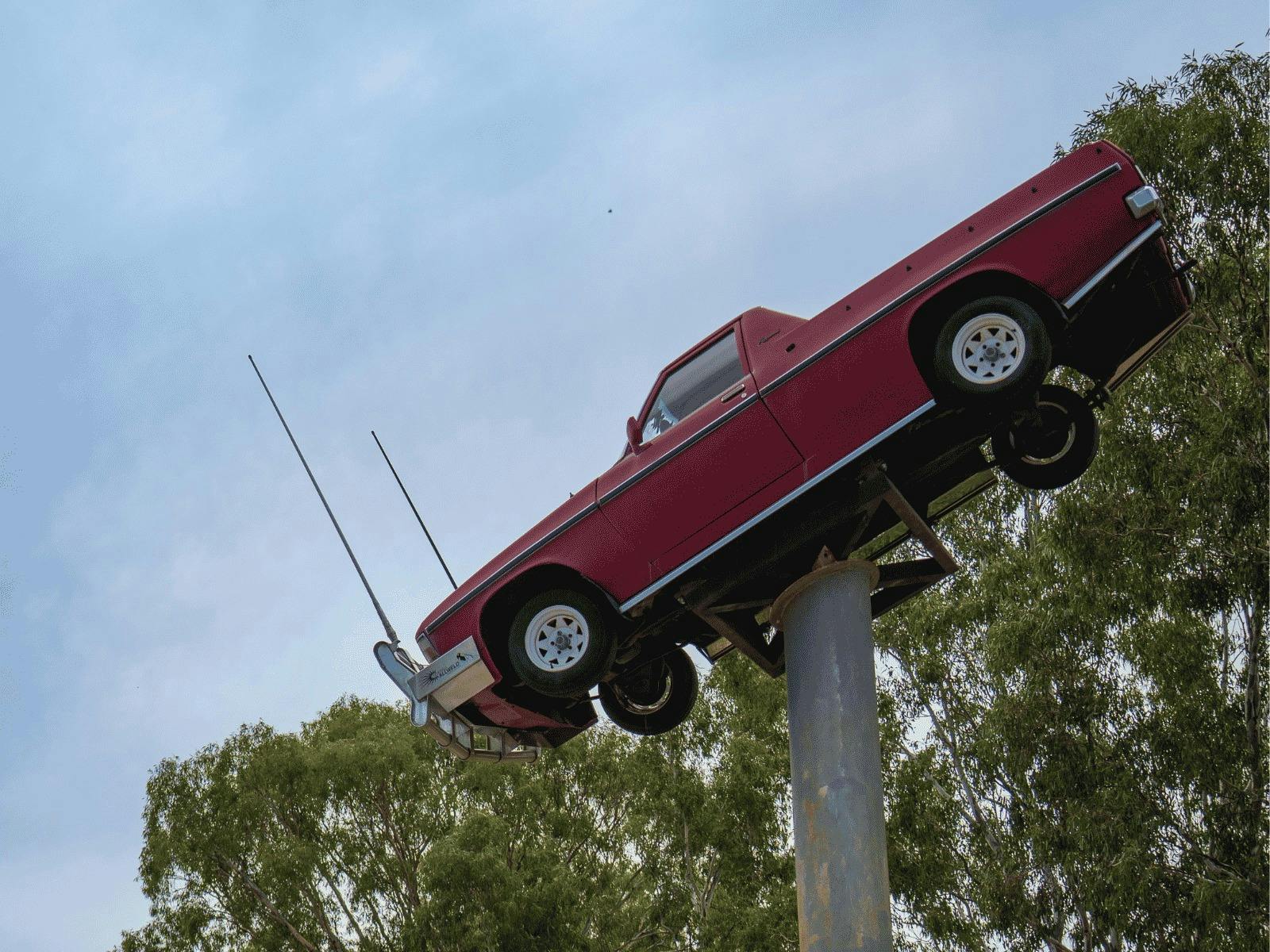 A red ute appears to be floating in the sky with gumleaves in the background
