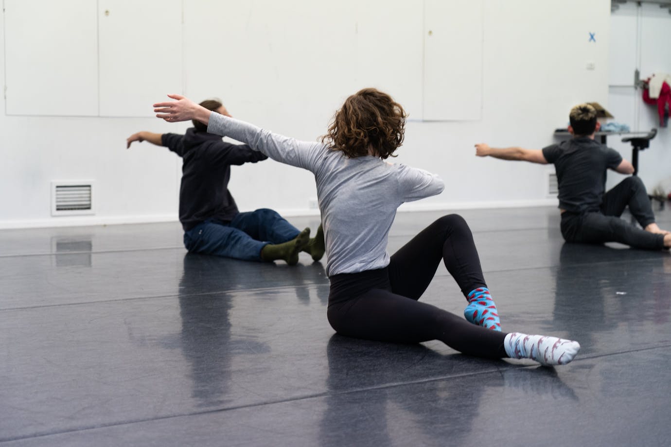 3 people are siting on the floor with thei legs outstretched. They are twisting away from the camera