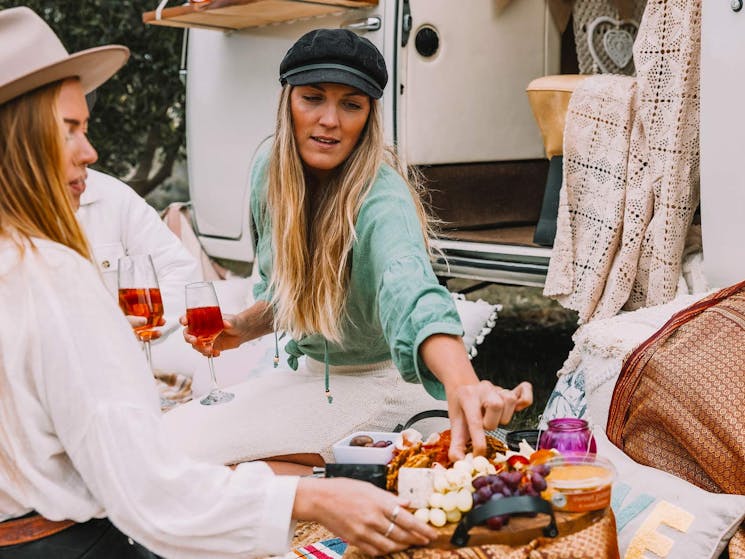 Two ladies nibbling on a grazing platter whilst sipping a glass of wine on a wine tour by the kombi