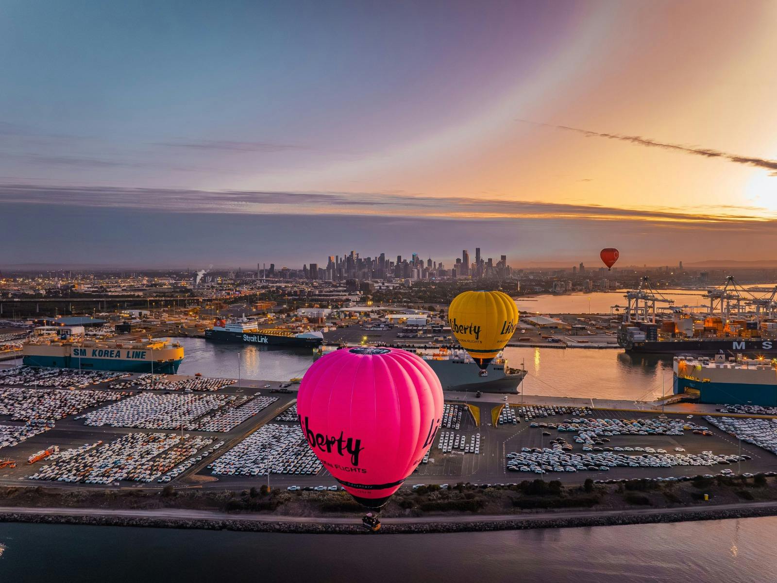 Pink and yellow branded hot air balloons floating over Melbourne city and Docklands