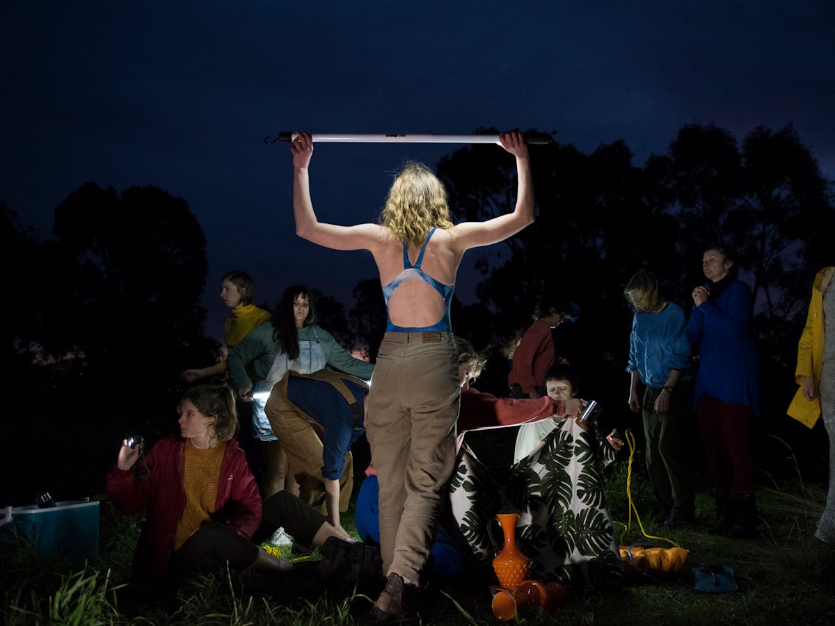a performer holds a bar above her head on a darkened stage
