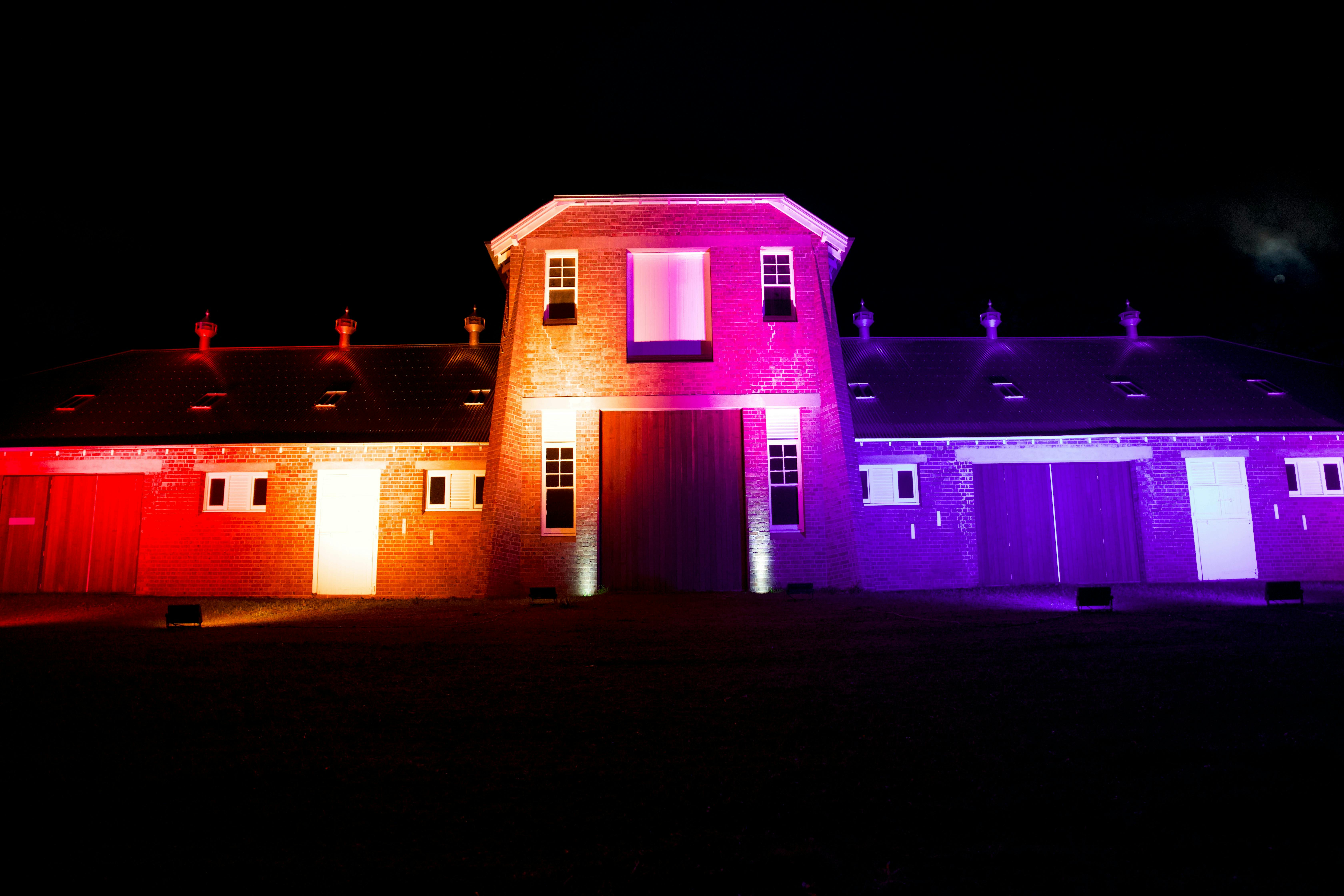 Brick building lit in red, pink, and purple light against a dark night sky.